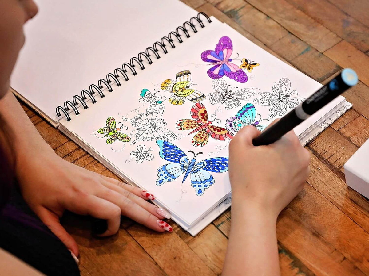 Mano che sfuma un disegno di farfalle colorate su un quaderno ad anelli con un marker Chameleon